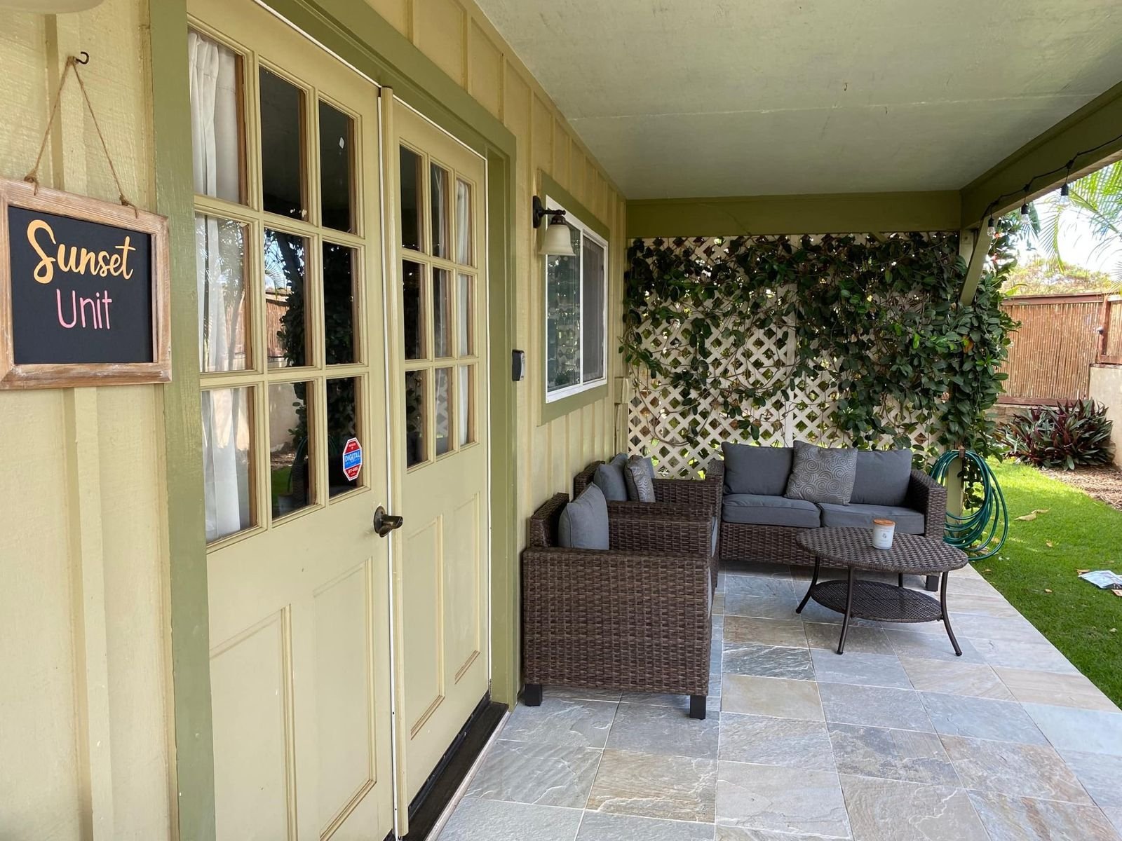 The covered lanai along the house with wicker seating and a chalkboard sign reading Sunset Unit.