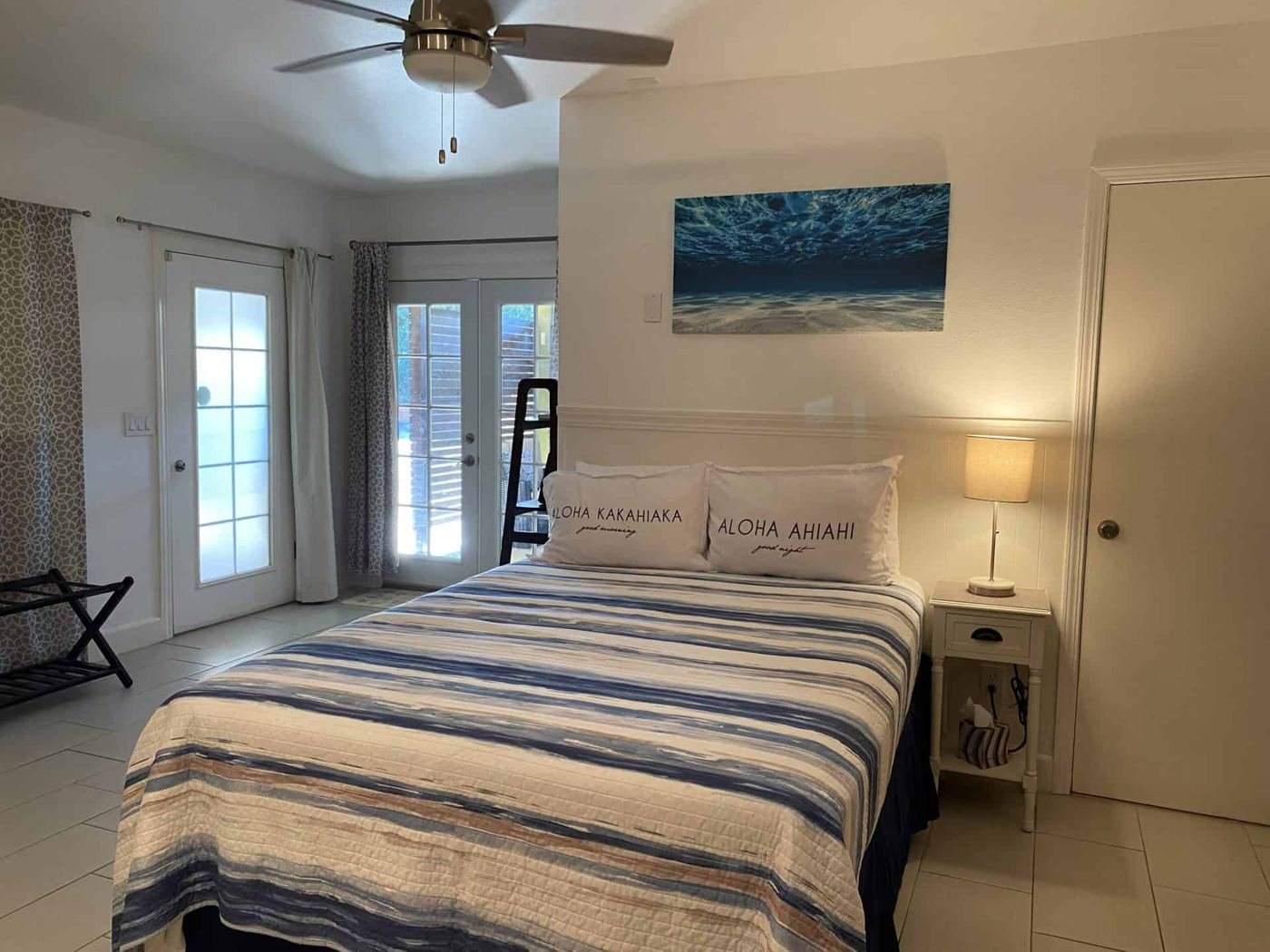 The Sunrise queen bed with striped bedding and Aloha pillows beside the lanai doors.