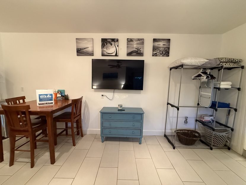 The Sunrise television on the wall above a blue dresser, with the dining table on one side and an open clothes rack on the other.