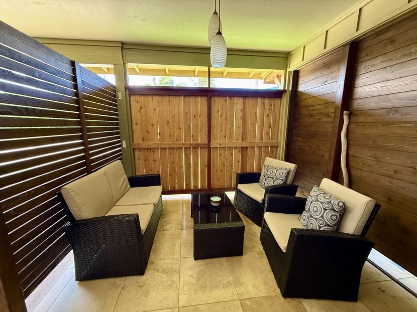 The Sunrise lanai with two wicker sofas and armchairs around a low table, screened by a bamboo blind and a wood fence.