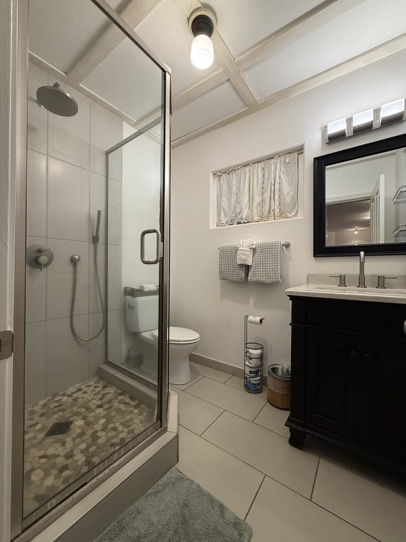 The whole Sunrise bathroom, with the glass walk-in shower on the left and the dark vanity and its black framed mirror on the right.