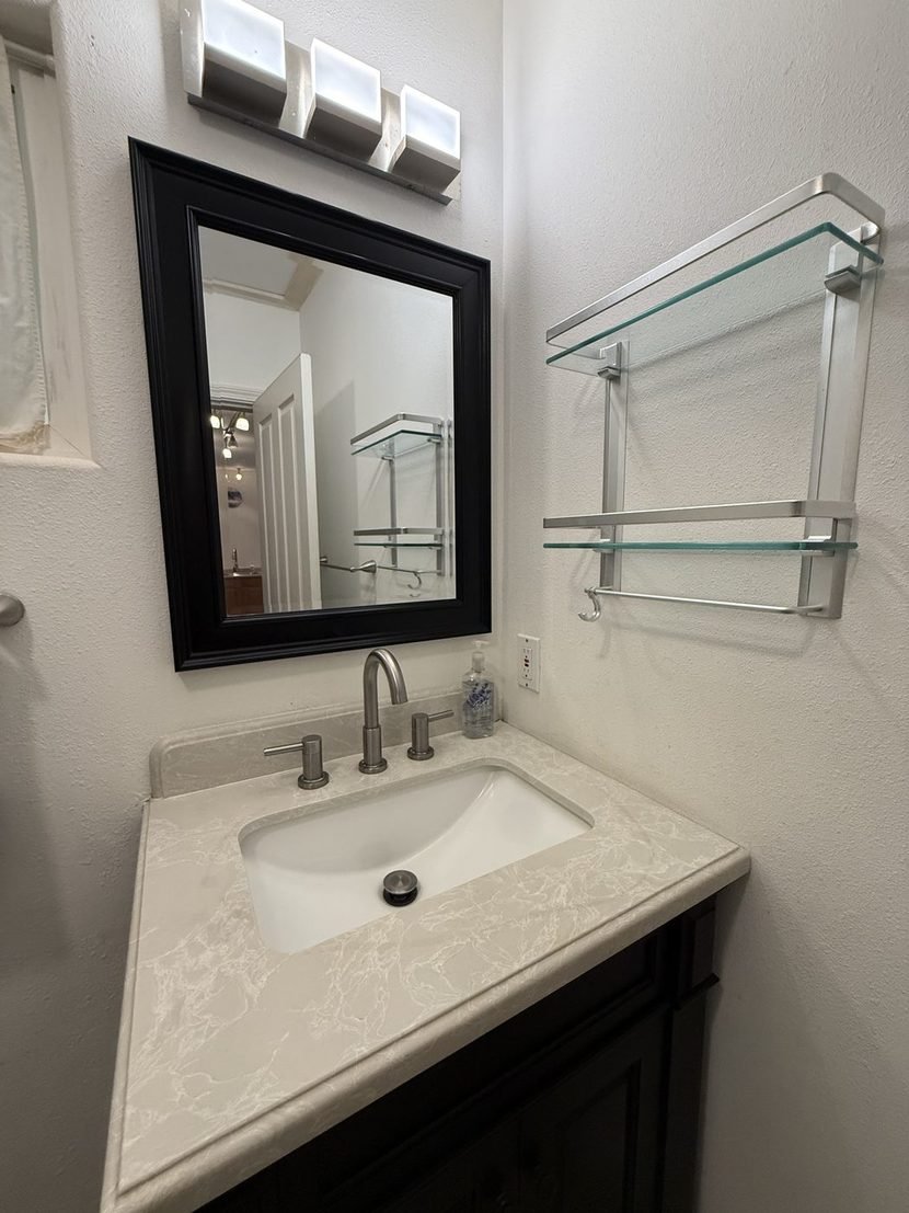 The Sunrise bathroom vanity: a black framed mirror, a glass shelf and a white sink in a marble top.