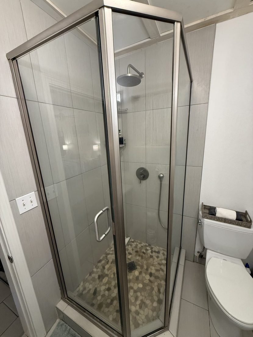 The Sunrise walk-in shower behind a clear glass door, with a rain head and a pebble tiled floor.