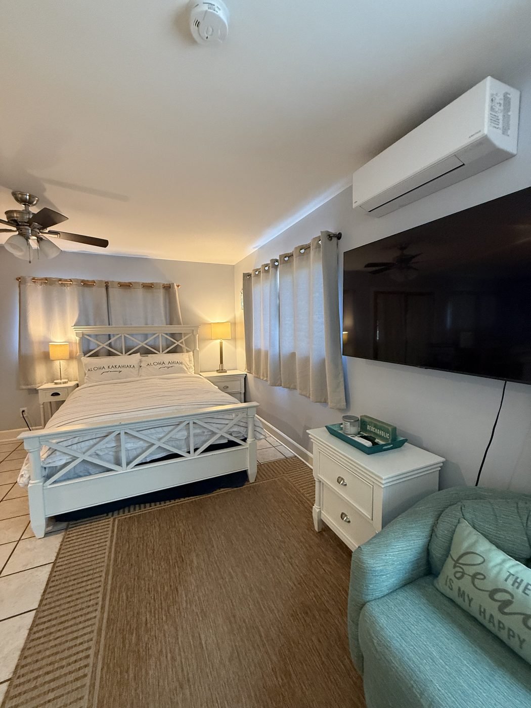 The Sunset queen bed with a white slatted headboard, beside a soft green armchair and the wall air conditioner.
