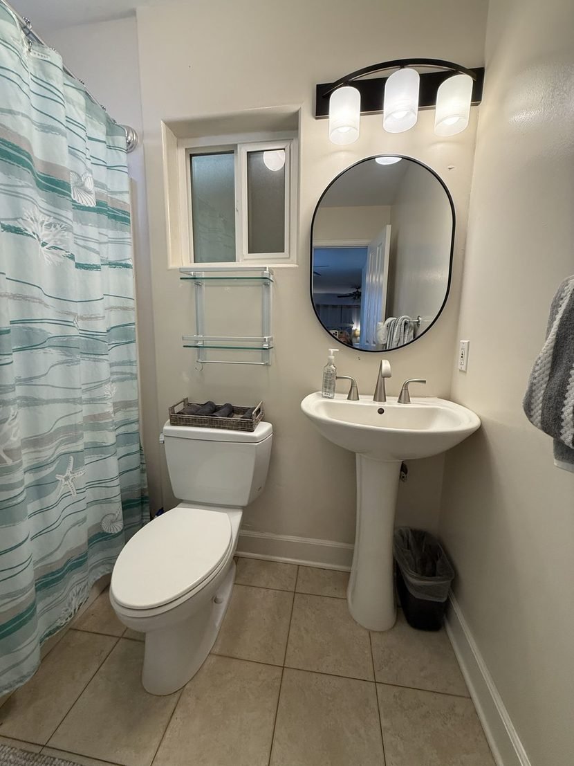 The Sunset full bath with the tub behind a striped curtain, a pedestal basin and an oval mirror.